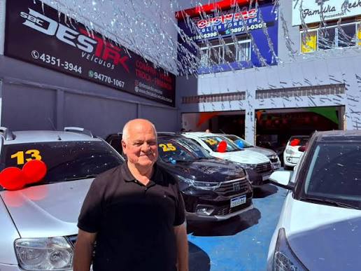 Proprietário da Destak Veículos em frente à fachada da loja, com carros do estoque ao redor
